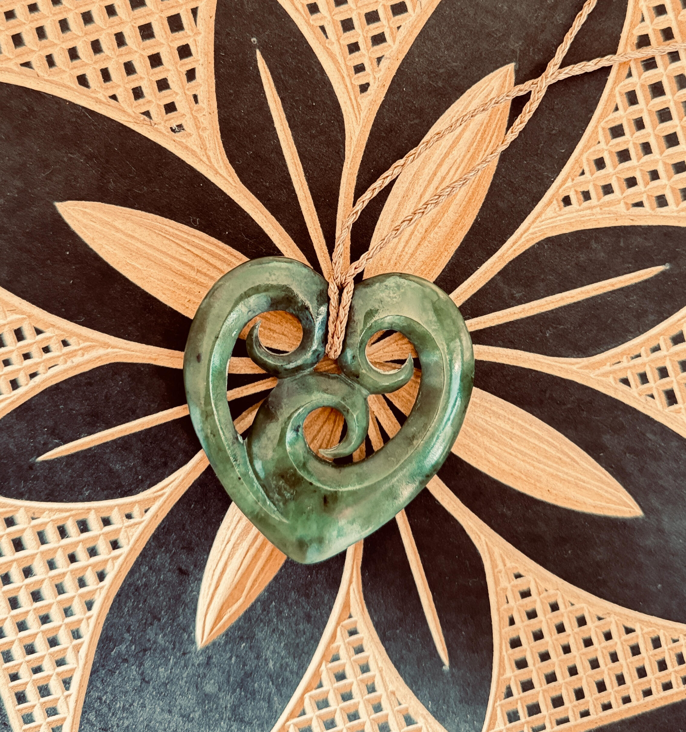 Taonga Image of a heart shaped pounamu taonga lying over a Samoan carving representing family.